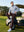 Model seated in a golf cart, wearing stretch plain everyday pants in dark brown with relaxed fit