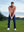Model on grass under blue sky, leaning on golf club, wearing quarter zip melange pullover in brick melange.